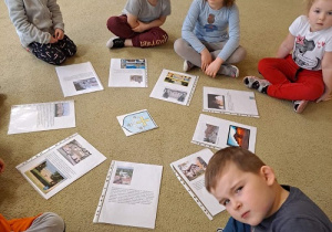 Dzieci siedzą na dywanie i ogladają zdjęcia.