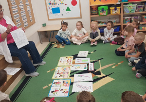 Dzieci siedzą w półkolu na dywanie